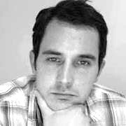 Black and white portrait of a man resting his chin on his hand, wearing a plaid shirt.